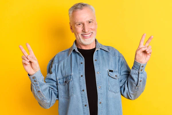 Photo of excited aged grandpa show v-sign wear jeans jacket isolated on vivid yellow color background — Stockfoto