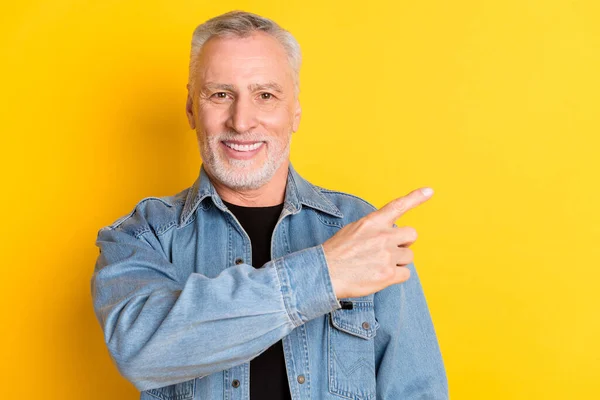 Photo of funny mature grandpa point empty space wear jeans jacket isolated on vivid yellow color background — Stockfoto