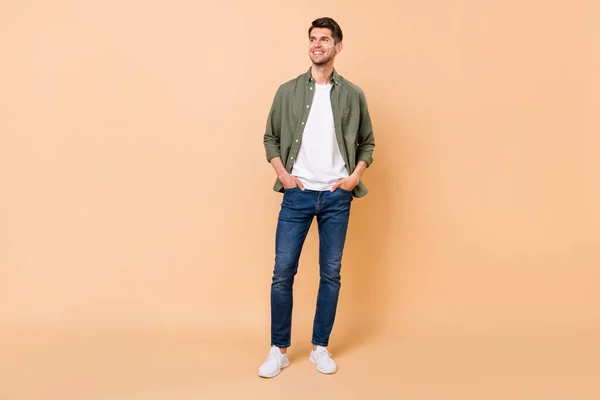 Full size photo of dreamy young man look empty space hold hands pockets jeans isolated on beige color background — ストック写真