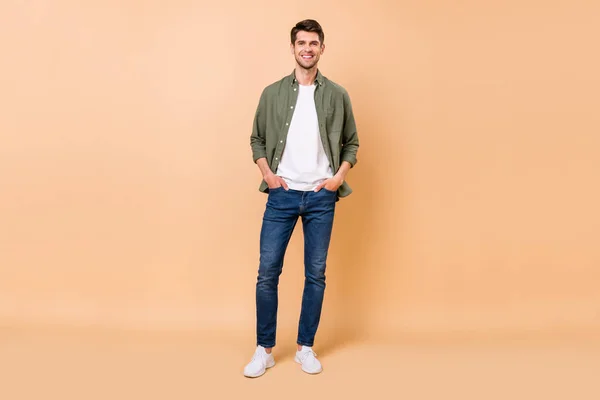 Full body photo of charming cheerful positive young man hold hands pockets isolated on beige color background — Stok fotoğraf