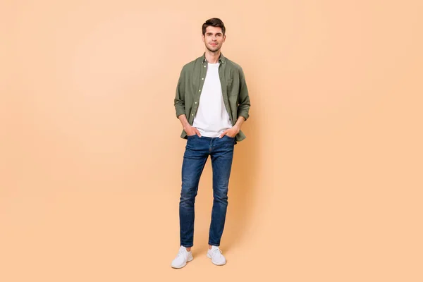 Photo of charming confident young guy dressed green shirt smiling walking arms pockets isolated beige color background — Stok fotoğraf