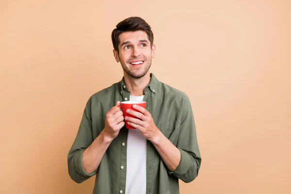 Foto de sonho muito jovem vestido camisa verde beber café olhando espaço vazio isolado cor bege fundo — Fotografia de Stock