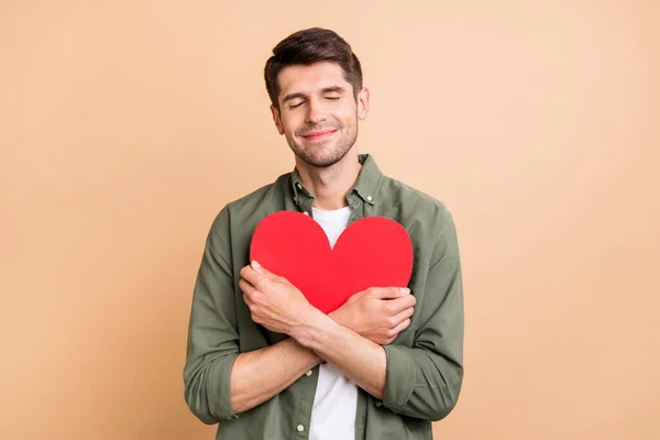 Photo of calm peaceful young happy man hug embrace red paper heart isolated on beige color background — 스톡 사진