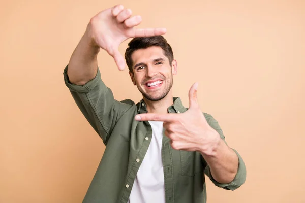 Foto van charmante vrolijke jonge vrolijke man maken vingers frame glimlach geïsoleerd op beige kleur achtergrond — Stockfoto