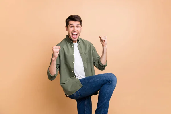 Foto van vrolijke positieve jonge man verhogen vuisten been winnaar vieren goed humeur geïsoleerd op beige kleur achtergrond — Stockfoto