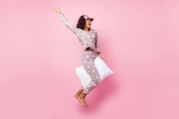 Photo of sweet funky wavy dark skin lady dotted sleepwear jumping high riding white pillow isolated pink color background — ストック写真