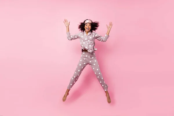 Photo of adorable funny curly dark skin woman dotted nightwear rising arms hands jumping high isolated pink color background — Stok fotoğraf