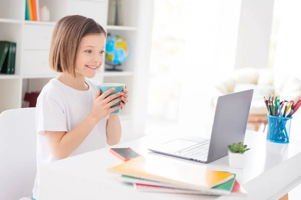 写真の肖像画の女の子はノートパソコンのお茶を飲みながらオンラインレッスンを見て笑顔 — ストック写真