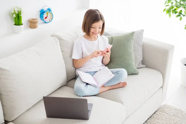 Küçük kız kanepede oturmuş cep telefonuyla internette geziniyor. — Stok fotoğraf