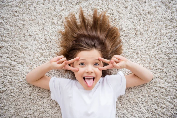 Foto di adorabile divertente piccola studentessa vestita di bianco t-shirt bastone fuori v-segni coprire gli occhi in casa casa casa stanza — Foto Stock