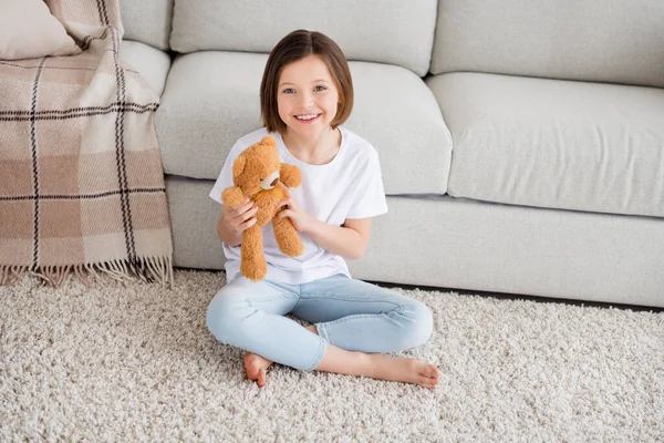 Full length foto di giovane allegra piccola ragazza felice sorriso positivo sedersi pavimento comfort giocare peloso orso giocattolo a casa — Foto Stock