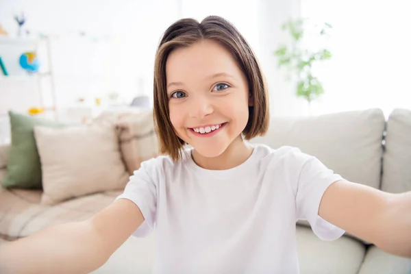 Φωτογραφία από αρκετά γοητευτικό μικρό σχολιαρόπαιδο ντυμένο λευκό t-shirt χαμογελώντας tacking selfie εσωτερικό δωμάτιο σπίτι — Φωτογραφία Αρχείου