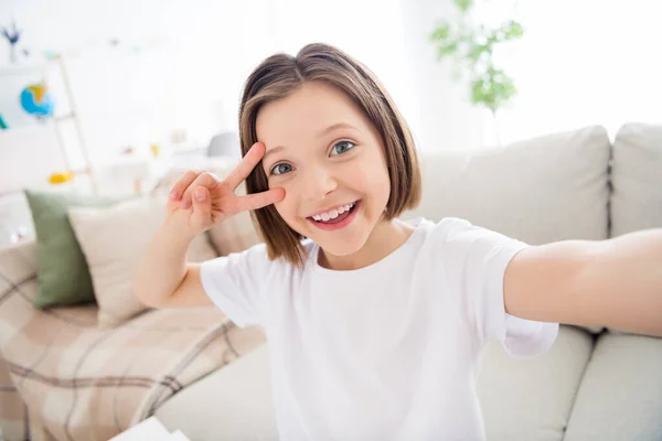 Φωτογραφία του νεαρού ελκυστική μικρό κορίτσι χαρούμενος θετικό χαμόγελο δείχνουν την ειρήνη δροσερό v-σημάδι κάνουν selfie σπίτι — Φωτογραφία Αρχείου