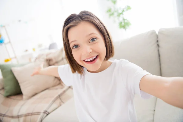 Foto de adorável doce escola menina desgaste branco t-shirt sorrindo gravação de vídeo convidando você dentro de casa casa quarto — Fotografia de Stock