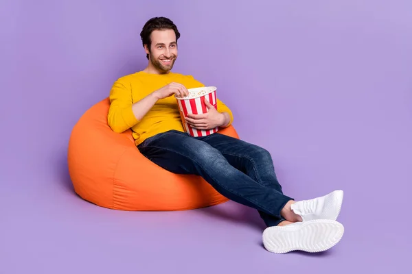 Portrait d'homme gai attrayant assis dans une chaise de sac s'amusant à manger du maïs regarder la télévision isolé sur fond violet pastel couleur pourpre — Photo