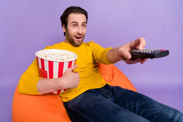 Портрет привлекательного изумленного веселого человека, наслаждающегося кукурузой, смотрящего сериал, изолированный на фиолетовом фоне из пастели. — стоковое фото