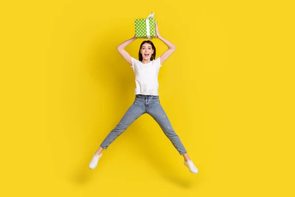 Vista completa del tamaño del cuerpo de la chica bastante alegre saltando sosteniendo la caja de regalos en la cabeza divirtiéndose aislada sobre un fondo de color amarillo brillante —  Fotos de Stock