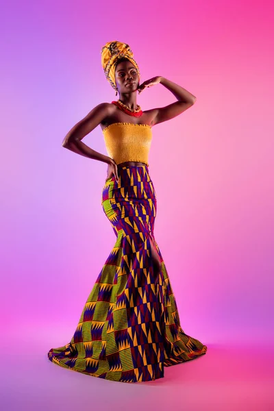 Foto em tamanho completo de mulher afro-americana atraente segurar mão rosto cintura desgaste vestido tribal isolado no fundo luz brilho — Fotografia de Stock