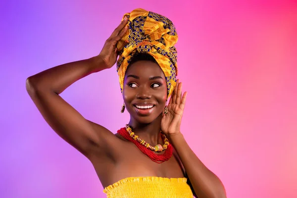 Foto de mujer afro americana joven mirada espacio vacío sonrisa toque ropa tribal aislado sobre fondo vibrante —  Fotos de Stock