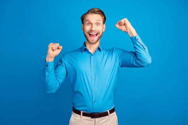 Фото молодої людини щаслива позитивна посмішка радійте перемозі екстатичні досягнення кулаки руки ізольовані на синьому кольоровому фоні — стокове фото