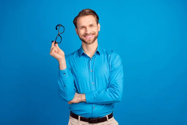 Фото молодого веселого человека счастливая положительная улыбка держать очки носить рубашку изолированы на синем фоне цвета — стоковое фото