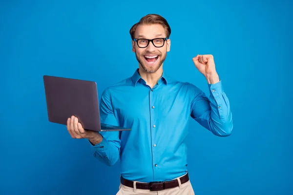 Фото молодого бизнесмена счастливой позитивной улыбкой использовать ноутбук радоваться победу кулаки руки изолированы на синем фоне цвета — стоковое фото