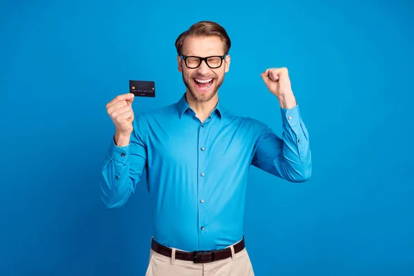흥분 한 젊은 남자의 사진 행복 한 미소 신용 카드 수입 이 파란 색 배경 위에 고립된 승리의 손을 기쁘게 하고 있다 — 스톡 사진