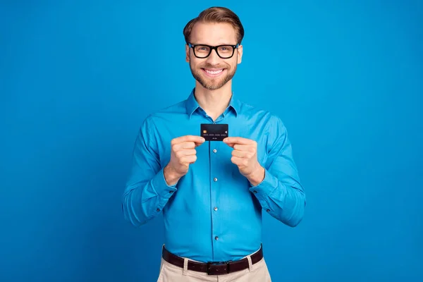 Foto de joven hombre de negocios feliz sonrisa positiva mantenga la tarjeta de crédito comprar compras aisladas sobre fondo de color azul — Foto de Stock