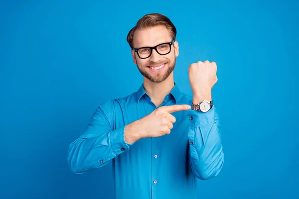 Fotografie mladého muže šťastný pozitivní úsměv ukazováček náramkové hodinky pozdě termín izolované přes modré barvy pozadí — Stock fotografie