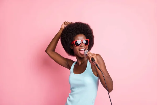 Foto de la encantadora piel oscura funky joven cantante de micrófono llevar gafas de sol karaoke aislado en el fondo de color rosa — Foto de Stock