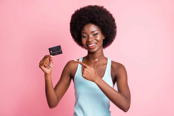 Foto de bonita morena afro-americana menina usar azul singlet apontar cartão de crédito dedo isolado no fundo cor-de-rosa — Fotografia de Stock