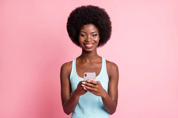 Fotografie optimistické pěkné brunetky kudrnaté dáma držet telefon nosit modrý top izolované na pastelové růžové barvy pozadí — Stock fotografie
