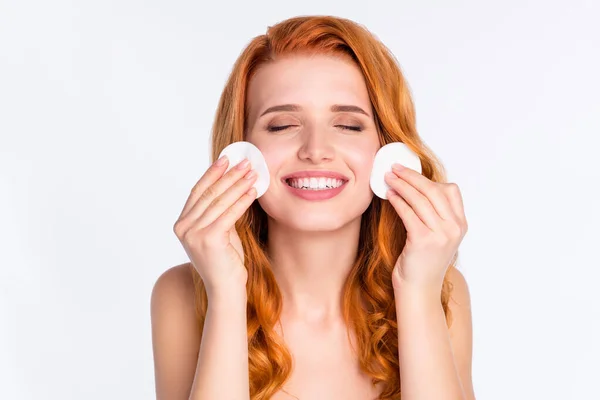 Foto retrato de modelo joven con pelo rojo rizado sonriente aplicando tóner con discos de algodón aislados sobre fondo de color blanco — Foto de Stock