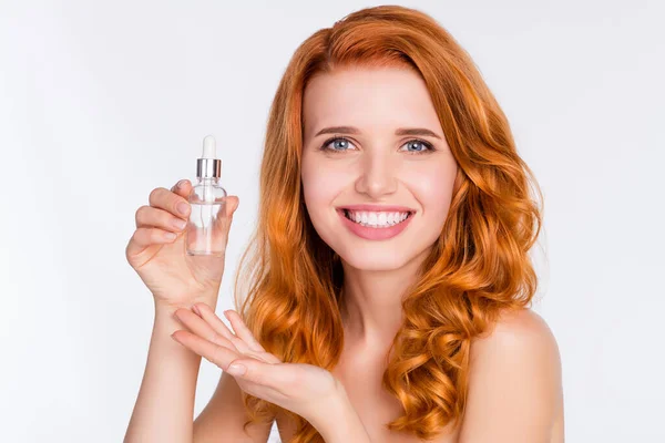 Foto retrato de menina bonita com cabelo de gengibre ondulado sorrindo mostrando garrafa com essência de soro para a pele isolada no fundo de cor branca — Fotografia de Stock