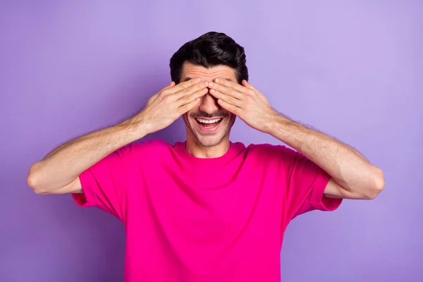 Fotografie legrační hravý mladý muž nosit růžové t-shirt ramena kryt oči izolované fialové barvy pozadí — Stock fotografie