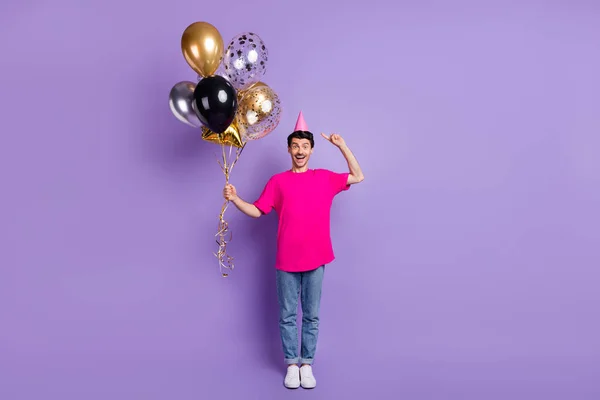 Foto de tamaño completo de joven feliz hombre positivo emocionado mantenga globos apuntar el dedo en la tapa del cono aislado en el fondo de color violeta —  Fotos de Stock