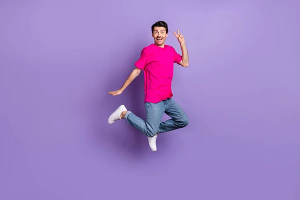 Full size photo of young happy cheerful excited smiling man jumping showing v-sign isolated on purple color background — Stock Photo, Image