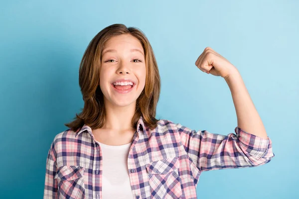 Foto de chica brillante fuerte de la escuela usar camisa a cuadros que muestra los músculos del brazo aislado fondo de color azul — Foto de Stock