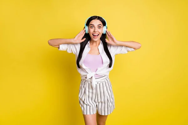 Foto de mujer joven feliz sorprendido escuchar música auriculares sonido impactado aislado en el fondo de color amarillo —  Fotos de Stock
