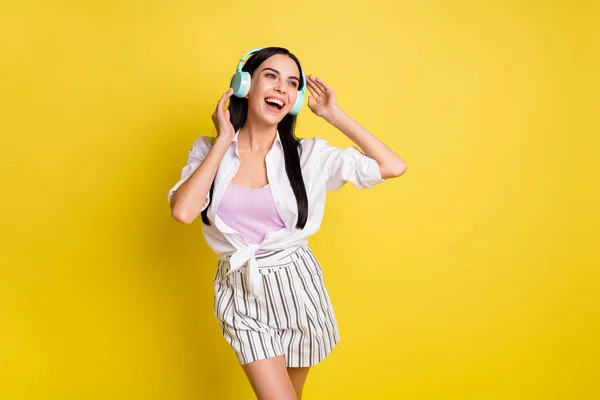 Fotografie ohromující šťastná mladá žena držet nosit sluchátka vypadají prázdný prostor sen izolované na žlutém pozadí barvy — Stock fotografie