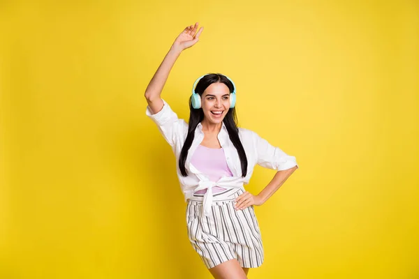 Foto di positivo funky giovane donna alzare le mani danza tenere mano vita usura auricolare isolato su sfondo di colore giallo — Foto Stock
