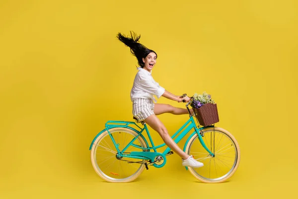 Foto lateral de perfil de tamanho completo de jovem encantadora menina encantadora com bicicleta de equitação de cabelo voador isolada no fundo de cor amarela — Fotografia de Stock