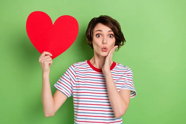 Retrato de menina surpreendente atraente segurando na mão forma de cartão amour pout lábios wow isolado sobre fundo de cor pastel verde — Fotografia de Stock