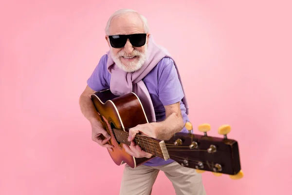Siyah güneş gözlüğüyle gitar çalan komik mutlu büyükbabanın fotoğrafı. Mutlu bir şekilde soluk pembe arka planda izole edilmiş. — Stok fotoğraf