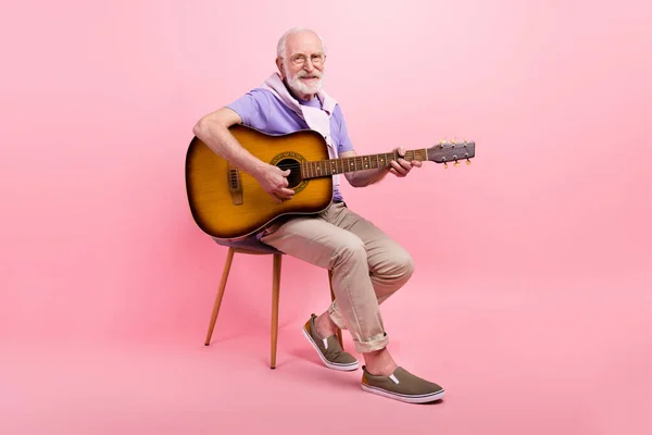Tam boy vücut büyükbaba gitar çalıyor. Sandalyede oturuyor. Pastel pembe arka planda izole edilmiş. — Stok fotoğraf
