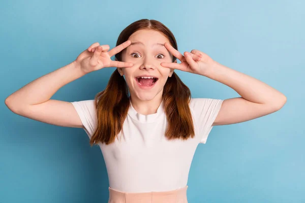 Foto de la persona sin preocupaciones divertidos dedos muestran v-signo cerca de los ojos boca abierta aislada sobre fondo de color azul —  Fotos de Stock