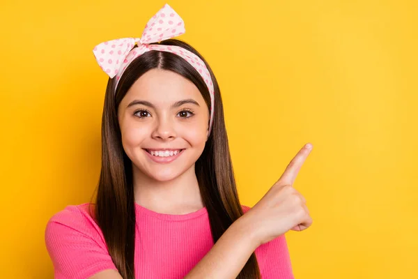 Foto de doce adorável menina da escola usar rosa t-shirt apontando dedo vazio espaço sorrindo isolado cor amarela fundo — Fotografia de Stock