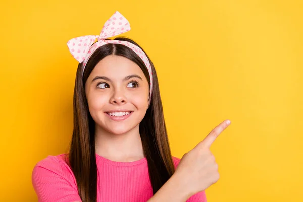 Foto av söt ganska liten skolflicka klädd rosa t-shirt ler pekar finger ser tomt utrymme isolerad gul färg bakgrund — Stockfoto