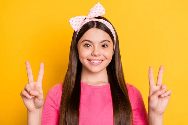 Foto de adorable linda niña de la escuela usar camiseta rosa que muestra dos signos de v sonriendo aislado color amarillo de fondo —  Fotos de Stock