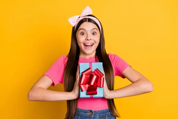 Foto de la encantadora chica de la escuela impresionada usar camiseta rosa sonriente celebración caja de regalo aislado color amarillo fondo — Foto de Stock